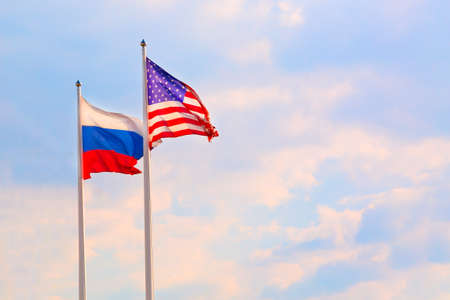 Russian Federation and United States of America flags on a blue sky background. Sanctions and...