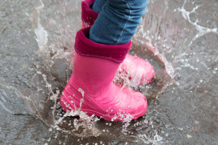 Autumn concept. The girl in pink boots jumping in puddles after rain outdoorsの写真素材