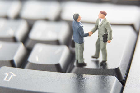 Business deal or agreement and success concept. Two miniature businessmen shaking hands while...