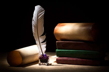 Literature concept. Old inkstand with feather near scrolls and books against black background. Dramatic light.の写真素材