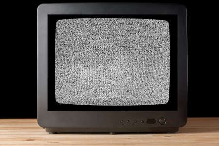 Old vintage TV set televisor on wooden table againt black background with no signal television grainy noise effect on the screen. No signal retro vintage television pattern. Interfering signal in analog televisionの写真素材