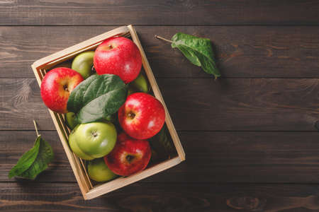 Ripe green and red apples in a wooden box with leaves on dark brown wooden rustic background. Autumn seasonal image with top viewの写真素材