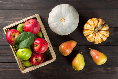 Pumpkins with ripe apples in a box and pears on dark wooden background. Autumn seasonal imageの写真素材