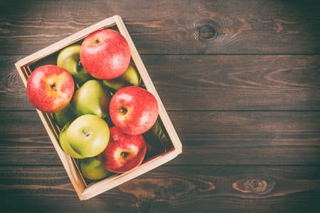 Ripe green and red apples in a wooden box on dark brown wooden rustic background. Autumn seasonal image with top viewの写真素材