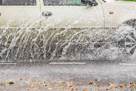 Car motion through big puddle of water splashes from the wheels on the street road.