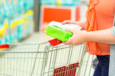 Closeup of woman hands with an item and shopping cart in supermarket. Shopping conceptの写真素材