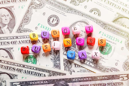 The words Budget, Business and Tax text on colorful wooden cubes on american dollar bank notes. Concepts of business management, financial plan or money savingの写真素材