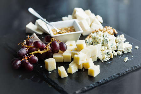 Restaurant cheese plate with sauce. Various types of cheeses with grape on black slate stone. Close up image with selective focus.の写真素材