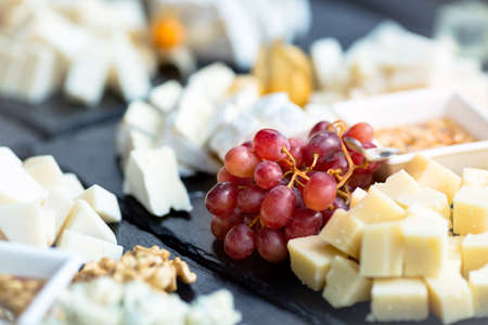 Restaurant cheese plate. Various types of cheeses with grape on black slate stone. Close up image...