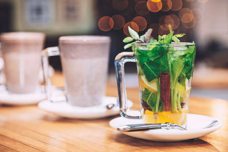 Cup of tea with mint, cinnamon and lemon of white plate. Nice red bokeh above the cup