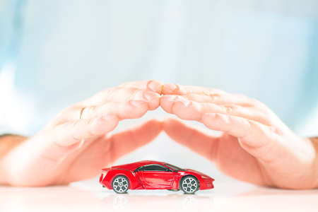 Male businessman hands above the small red miniature car. Car insurance concept