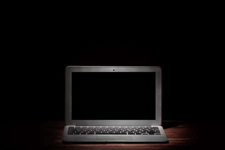 One silver modern laptop on wooden table in a dark room on black background. Nice mockup for your IT project. Dramatic lightの写真素材