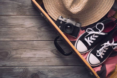 Summer holidays and vacation travel concept. Vintage camera, straw hat and sneakers in old suitcase...
