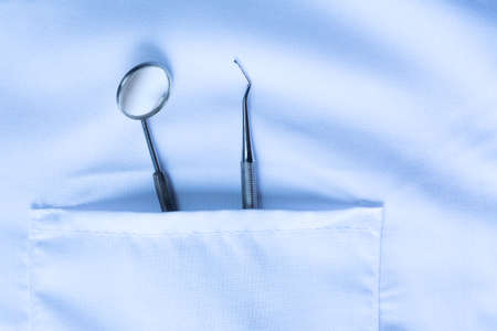 Closeup of dental tool and a mirror in white medical uniform pocket. Blue toned. Dental hygiene...