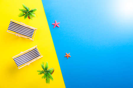 Miniature beach with deck chairs, palms and starfish on the colorful backgeound. Yellow and blue. Sand and ocean. Tropical resort and vacation conceptの写真素材