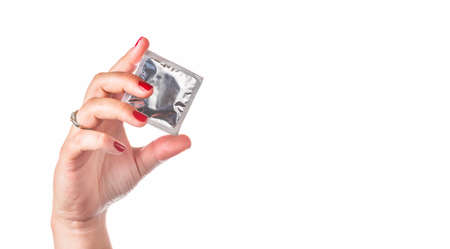 Condom in female hand with red nails isolated on white background. Prevent infection and control the birth rate. Copy space for text. Focus on condom.の写真素材