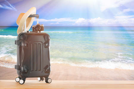 Summer holidays concept. Suitcase baggage with straw hat and retro camera against sandy tropical beach and turquoise water ocean. Blue sky and sunlight.の写真素材
