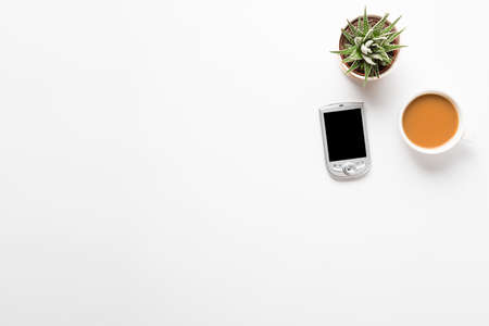 Top view of empty office desk. Green plant in a pot, cup of coffee and pocket communicator smart...
