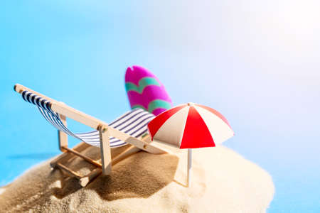 Miniature beach with deck chair, umbrella, parasol and surfboard on tropical islands sand surrounded by water. Tropical resort and vacation conceptの写真素材