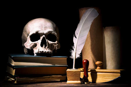 Drama or theater and literature concept. Old inkstand with feather near scrolls with skull on books...