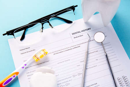 Dental history form with professional steel dental instruments, mirror, white tooth model and dental floss near toothbrush and glasses. Dental health and teethcare conceptの写真素材