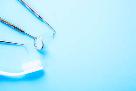 Dentist tools. Professional steel dental instruments with a mirror and toothbrush on blue background with free space. Dental health and teethcare conceptの写真素材
