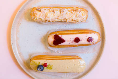 Group of french delicious colorful dessert eclair on plate and pink background.
