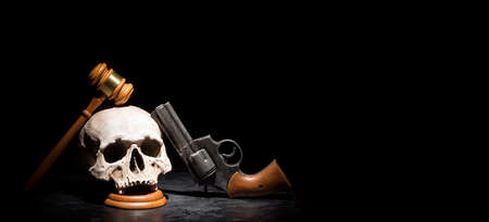 Legal law, justice and murderment crime concept. Wooden judge gavel hammer on human skull with revolver gun pistol against black background. Free spaceの写真素材
