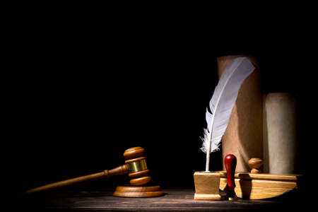 Wooden judge gavel hammer, old inkstand with feather quill, blotter, seal near scrolls against black...
