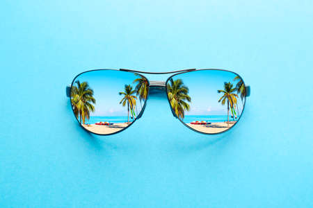 Summer vacation concept. Sunglasses with ocean beach and palms on blue backgroundの写真素材