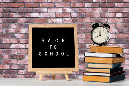 Back to school words on a letter board with books and vintage alarm clock against brick wall...