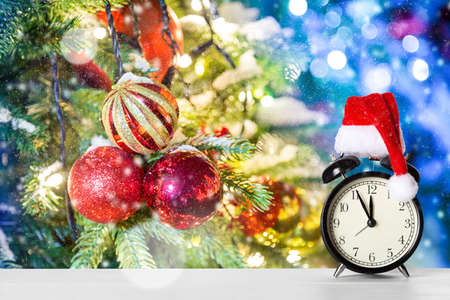 Retro alarm clock with Santa Claus hat against amazing Christmas tree background with Christmas...