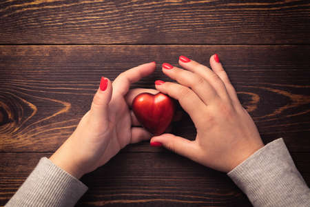 Health, medicine and love concept. Female hands with red nails holding heart on wooden background