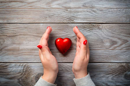 Health, medicine and love concept. Female hands with red nails and decorative heart on wooden backgroundの写真素材