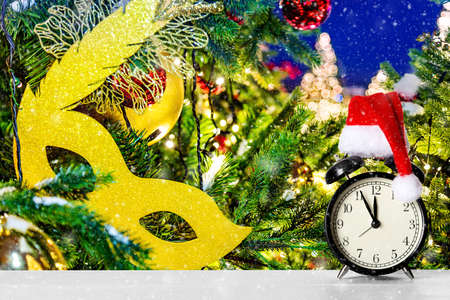 Retro alarm clock with Santa Claus hat against amazing Christmas tree background with Christmas toys, mask and lights. Merry Christmas or happy New Year card with snow.の写真素材
