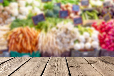 Blurred fresh vegetables at market with empty rustic wooden planks on the foreground. Can be used for advertise products. Mockup imageの写真素材