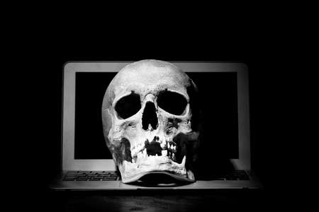 Cybercrime or hacking concept. Laptop in dark room under beam of light with a skull. Idea of virus or worm program cyber attackの写真素材