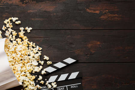 Cinema concept. Popcorn in a box and movie clapper on wooden background top view. Free spaceの写真素材