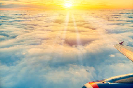 Beautiful sunrise sky above clouds with aircraft wing and engine. View from airplane window.