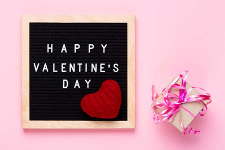 Valentines Day concept mockup. Happy Valentines day words on black letter board with a gift and decorative red heart on pink backgroundの写真素材