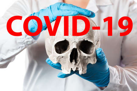 Coronavirus Covid-19 concept. Doctor in rubber gloves holding human skull and words COVID-19