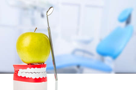 Dental mirror near green apple on human jaw model against dental chair background. Oral dental hygiene. Free space.の写真素材