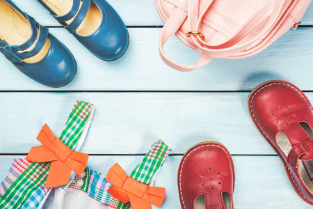 Little girl accessories. Pink bag with colorful dress and red blue shoes on blue pastel wooden background. Top view.の写真素材