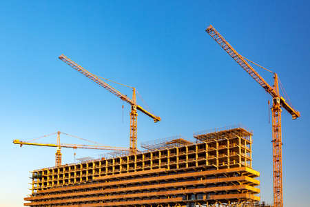 Industrial and construction concept. Construction site with modern building and cranes against blue...