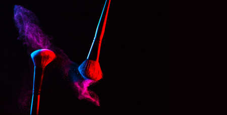 Make up cosmetic brushes with powder blush explosion on black background. Skin care or fashion concept. Nice red and blue neon lighting. Free space.の写真素材