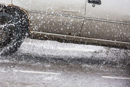 Car motion through big puddle of water splashes from the wheels on the street road