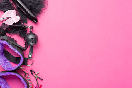 Intimate sex games. BDSM Tools dildo vibrator, female panties, gag, nipple clamps and handcuffs on red pink background. Free space for your text.の写真素材