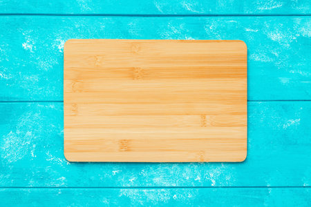 New rectangular wooden bamboo cutting board on blue wooden table. Mockup for food project. Top view.