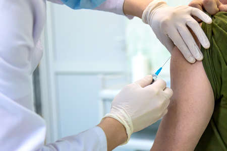 Vaccination concept. Doctor in rubber gloves injecting syringe with vaccine. Close up with selective focus.の写真素材