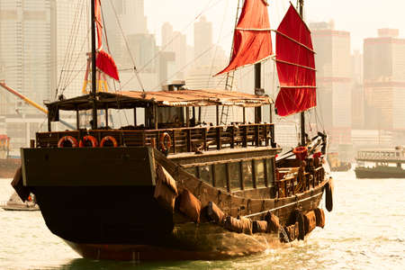 Old wooden tourist junk ferry boat in Victoria Harbor against famous Hong Kong island view with skyscrapers.のeditorial素材
